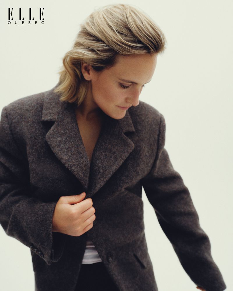 Woman in a gray blazer standing indoors against a white background and with the Elle Quebec logo at the upper left corner.