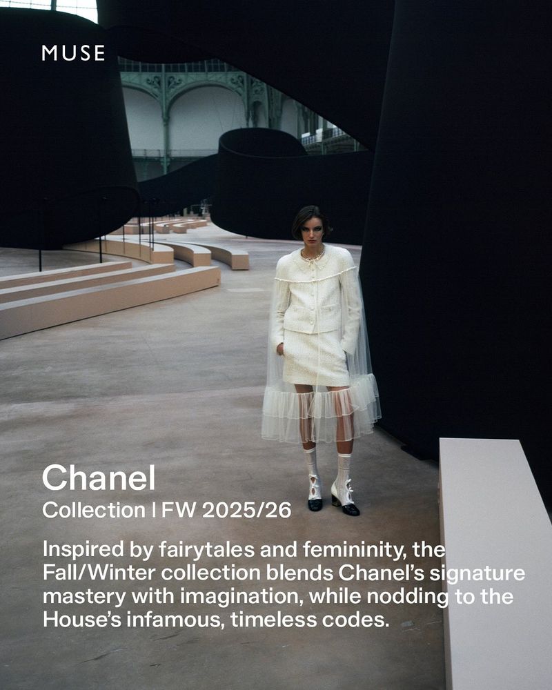 Fashion shoot in a grand hall featuring a woman in a white Chanel skirt suit with sheer details, posed against a backdrop of abstract black shapes.