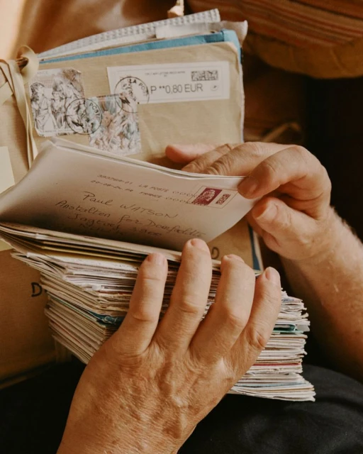 Close-up on hands holding a stack of old letters with various stamps and handwritten addresses, evoking a sense of nostalgia.