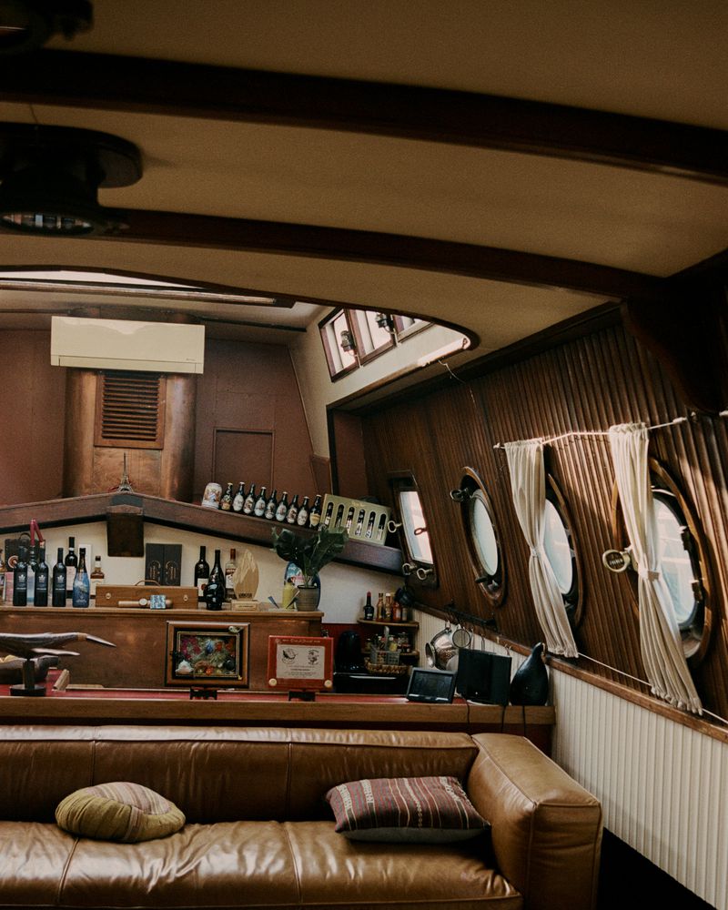 Interior view of a boat cabin featuring a leather couch, wooden walls, and round windows, offering a cozy nautical ambiance.