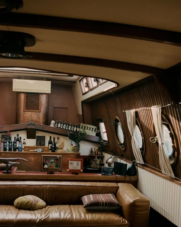 Interior view of a boat cabin featuring a leather couch, wooden walls, and round windows, offering a cozy nautical ambiance.