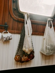 Mesh produce bags filled with onions hanging from hooks inside a wood-paneled boat cabin with a porthole window.