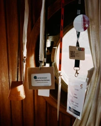 Lanyards and press badges hanging in front of a round ship porthole against wooden paneling.