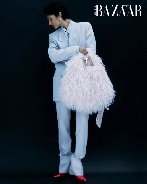 Full-length studio shot of a model in a light blue suit holding a fuzzy lavender handbag against a dark background, fashion editorial.