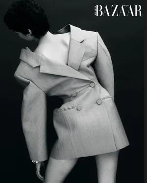 Model wearing a structured grey blazer backward against a dark background for Harper's Bazaar Arabia