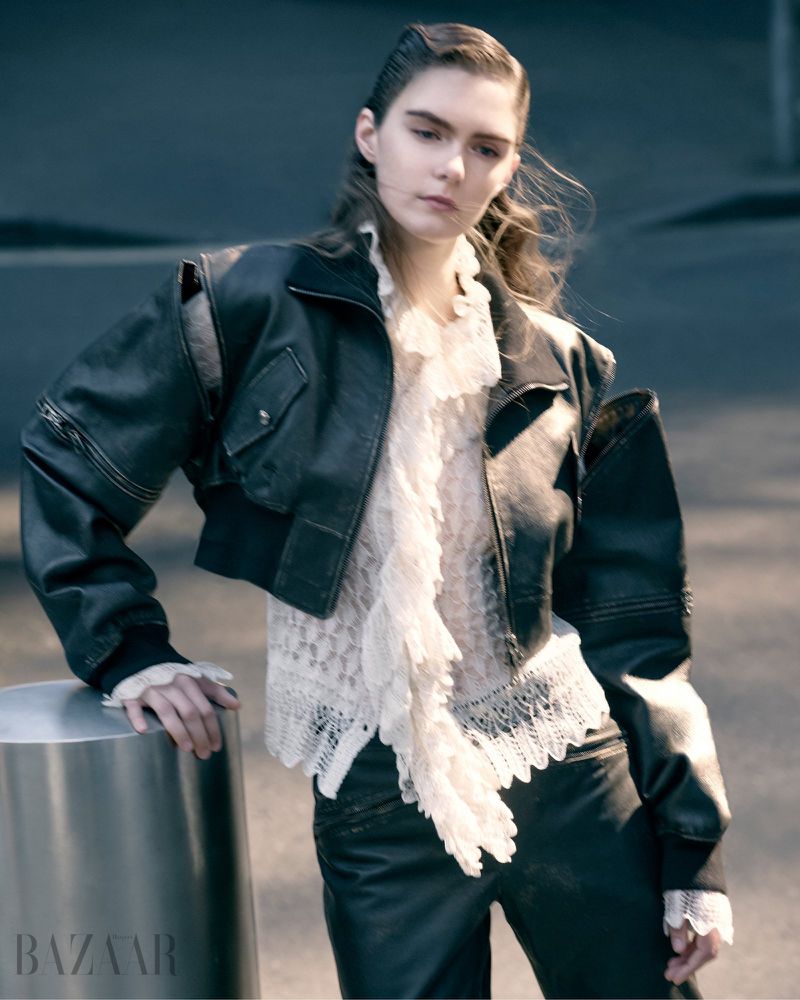 Fashion shot of a woman in a black leather jacket, a lace blouse, and leather pants posing outdoors in an urban setting.