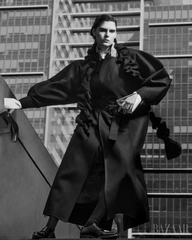 Model in a black coat standing on a staircase against an office building exterior background