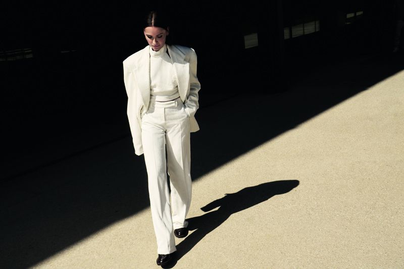 Almudena Fernandez in a white suit walking on paved ground casting a long shadow for Mujer Hoy fashion editorial.