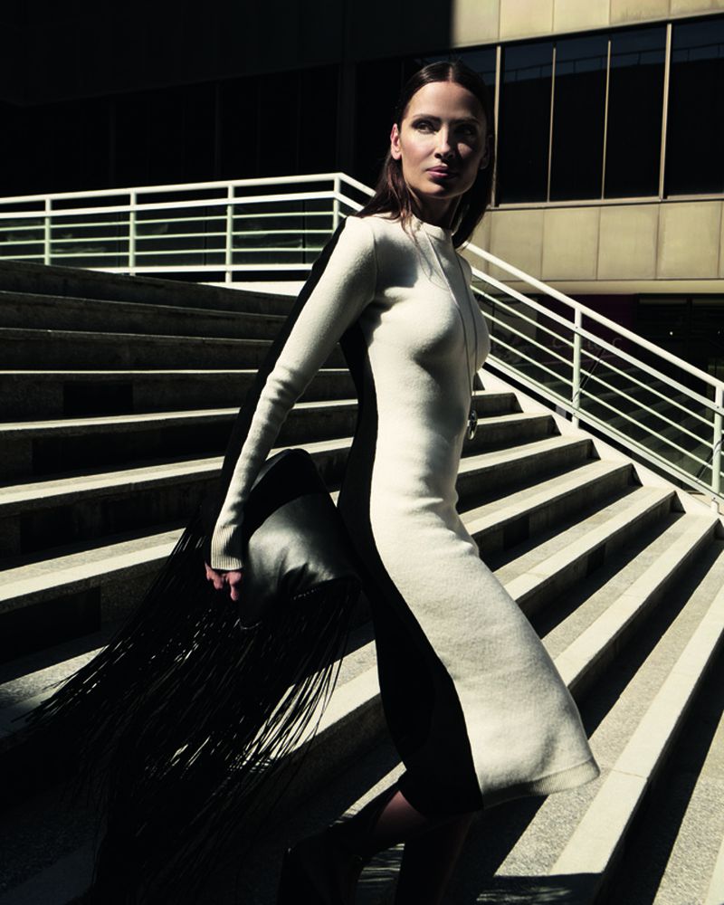 Elegant woman in a black and white dress descends concrete stairs in an urban setting with natural light creating shadows.