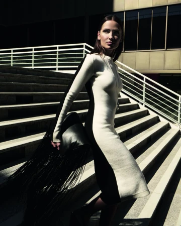 Model Almudena Fernandez walking down outdoor stone stairs wearing a long two tone dress holding a fringed black bag