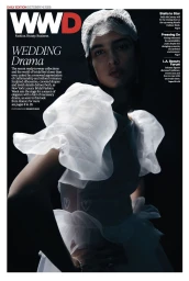 Model Silvia Perdomo wearing a sheer white bridal dress with ruffled organza sleeves and lace headpiece on a WWD cover against black.