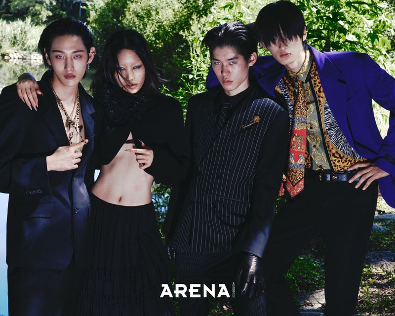 Four Asian fashion models pose outdoors in stylish suits and jackets in a medium shot with lush greenery in the background.