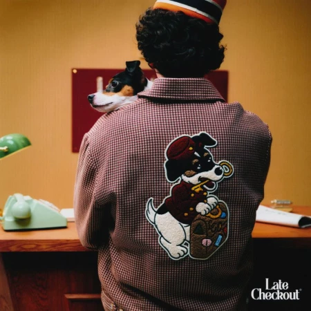 Person in bellhop uniform with dog on shoulder inside hotel, featuring embroidered dog graphic on back of jacket and vintage telephone.