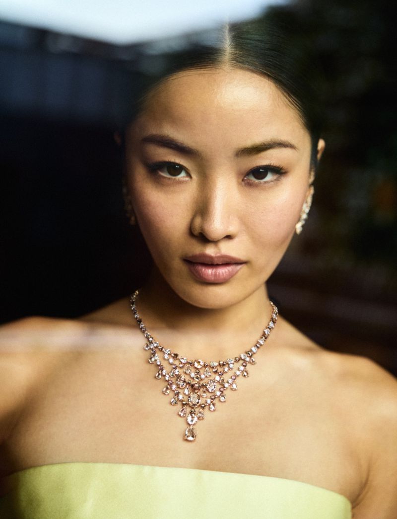 Portrait of a glamorous Asian woman wearing a crystal necklace and earrings, posing in a studio with neutral background and soft lighting.
