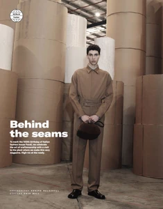Sereto Boardman posing in a tan utilitarian collared shirt and trousers holding a brown pouch in an industrial paper roll facility.