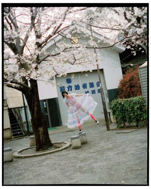 Woman in a colourful dress strikes a pose on concrete blocks beneath a blooming cherry tree with a building in the background.
