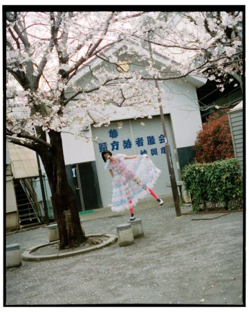 Woman in a colourful dress strikes a pose on concrete blocks beneath a blooming cherry tree with a building in the background.