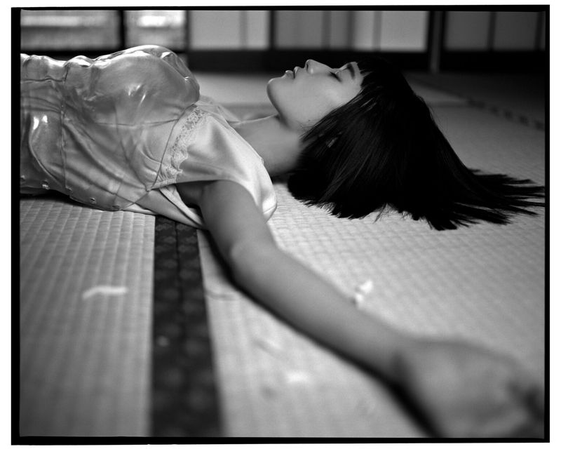 Black and white portrait of a woman lying on a tatami mat, hair spread, wearing silk top, side view.