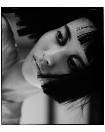 Close-up black and white portrait of a woman with a sharp blunt black bob and micro bangs looking toward the camera.
