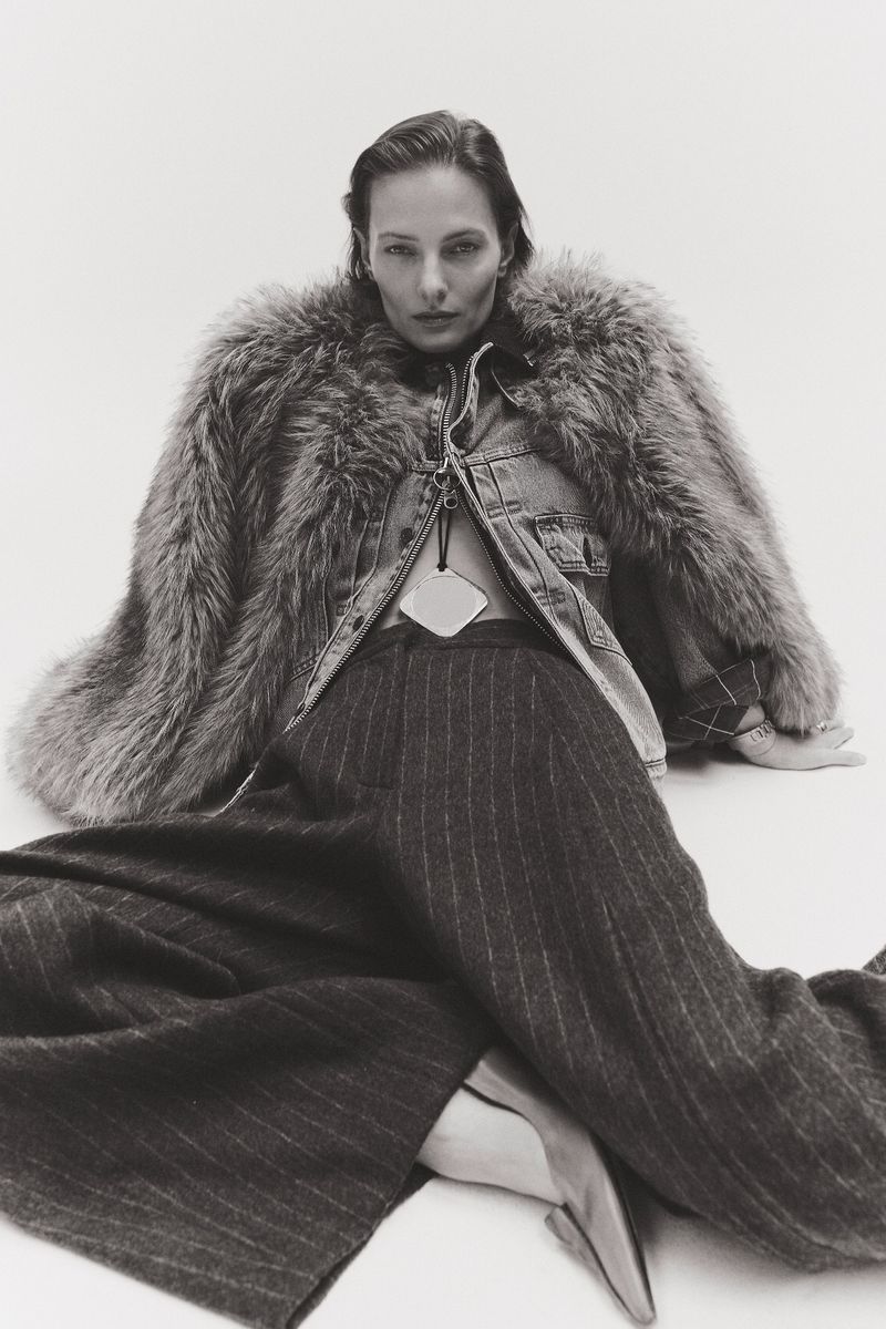 Woman poses in pinstripe pants, heels, denim jacket and faux fur coat against white background in fashion portrait.