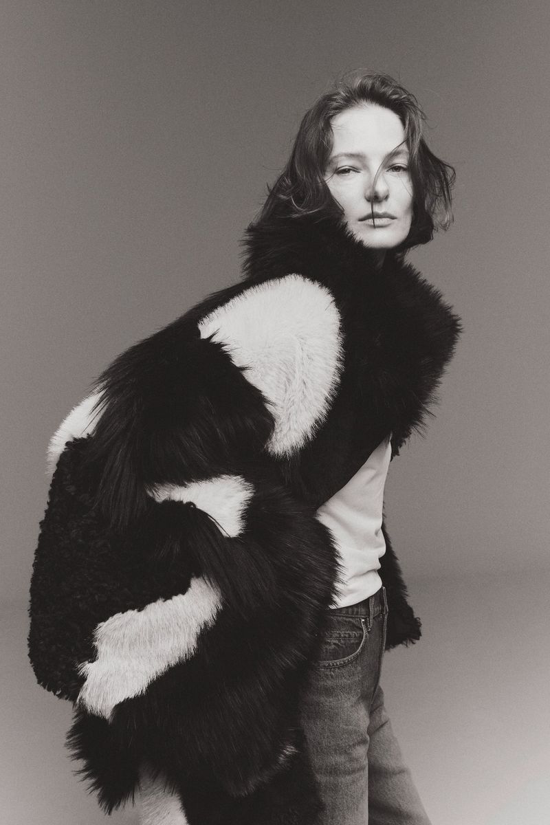 Monochrome portrait of a woman in a striped black and white coat, gazing at the camera with a neutral expression in a studio setting.