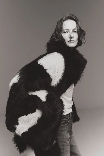 Model Tanya Ruban posing in a black and white faux fur coat, white shirt, and jeans against a neutral studio backdrop.