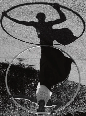 Monochromatic outdoor shot of person holding hoop with arms extended while upside down, shadow visible on pavement surface.