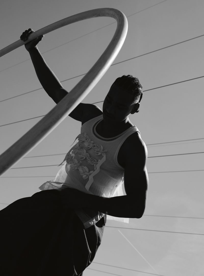 Black and white image of a person holding a curved bar, wearing a tank top, silhouetted against a bright sky with overhead power lines.