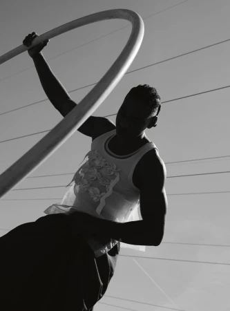 Black and white portrait of a person holding a curved metal bar outdoors with faint horizontal lines in the background sky.