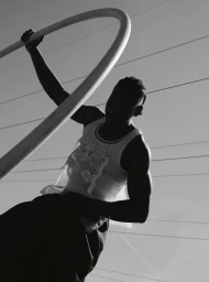 Black and white portrait of a person holding a curved metal bar outdoors with faint horizontal lines in the background sky.
