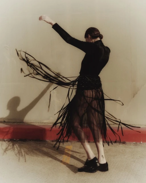 Adult woman in flowing black dress dances indoors with flowing skirt, wearing long sleeves and dark shoes in a fashion pose.