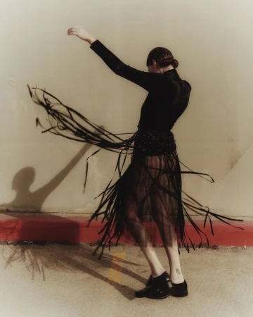 Adult woman in flowing black dress dances indoors with flowing skirt, wearing long sleeves and dark shoes in a fashion pose.