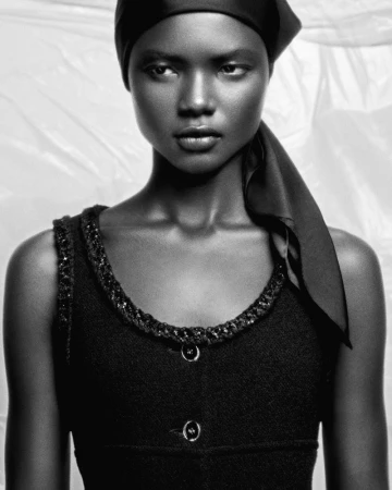 Monochrome portrait of an African woman in a dark, sleeveless top and headscarf against a soft, out-of-focus white background.