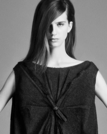 Black and white portrait of a woman wearing a dark dress. The image shows her upper body, arms down at sides, and long hair.