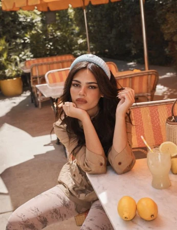 Woman wearing a blue headband and tan shirt sitting at an outdoor cafe table with a drink and lemons.