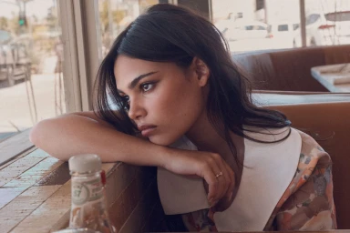 Close-up of a dark-haired woman resting her head on her arm inside a booth at a diner.