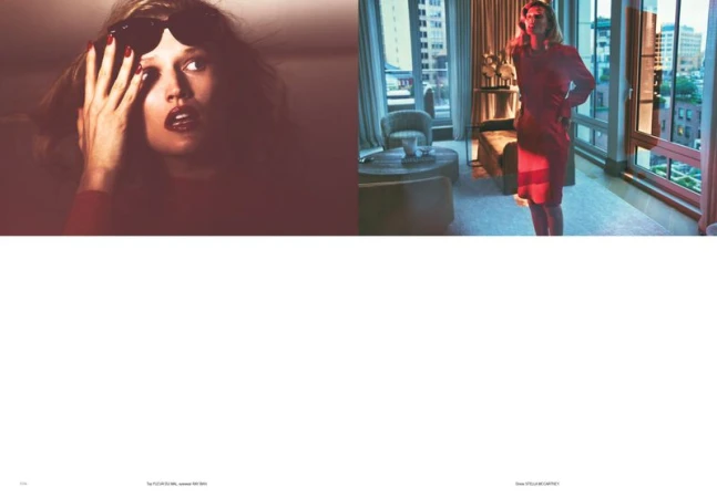Fashion editorial shot of a blonde woman in a red dress, captured indoors with a city skyline visible through a large window.