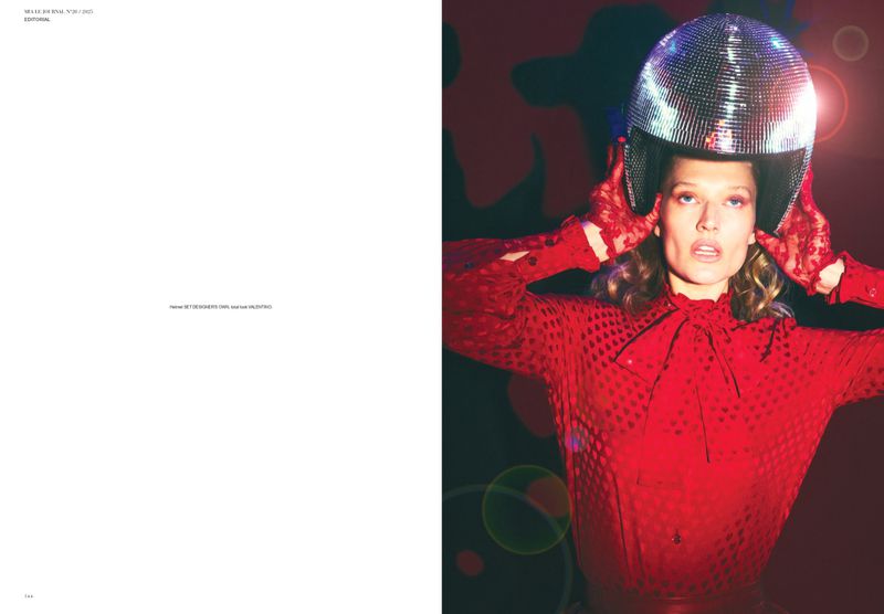 Woman in a shiny disco ball helmet, red blouse, and red lace gloves poses against a dark background with bright circles of light.