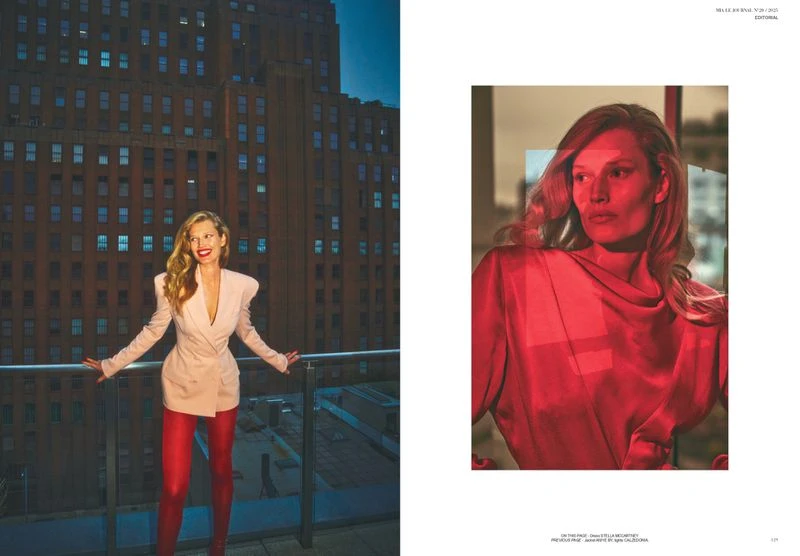 Fashion editorial shot of a smiling woman in a blazer dress, red leggings, and high heels, posing on a balcony with a cityscape backdrop.