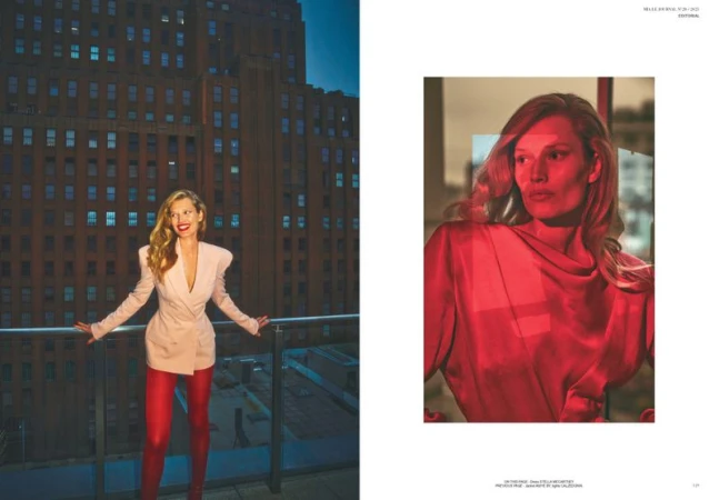 Fashion editorial shot of a smiling woman in a blazer dress, red leggings, and high heels, posing on a balcony with a cityscape backdrop.