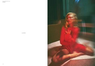 Model Toni Garrn in a red long-sleeve dress seated behind a fluted ribbed glass partition in an editorial magazine spread.