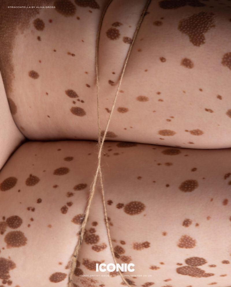 Close-up, stylized image of a body with skin markings and a light brown rope. The aesthetic evokes a surreal, textured feel.