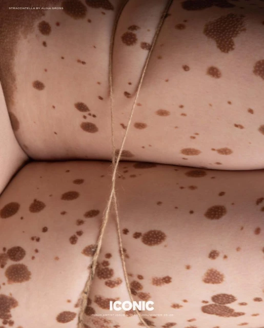 Close-up, stylized image of a body with skin markings and a light brown rope. The aesthetic evokes a surreal, textured feel.