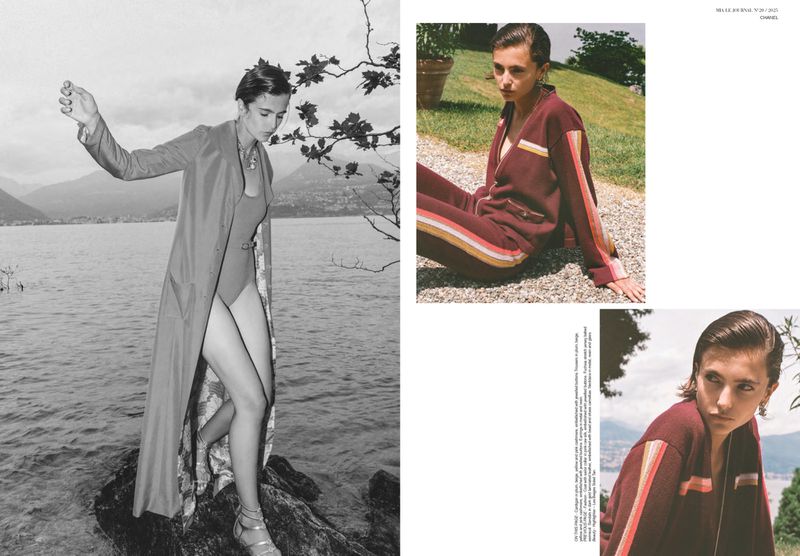Editorial fashion shot of a woman in a swimsuit and long coat standing on rocks by a lake with mountains in the background.