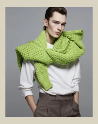 Model wearing a white crewneck sweater and bright green sweater draped over shoulders against a grey backdrop