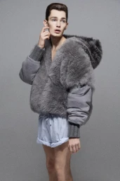 Model wearing a fuzzy grey hooded jacket and striped shorts against a grey textured studio backdrop