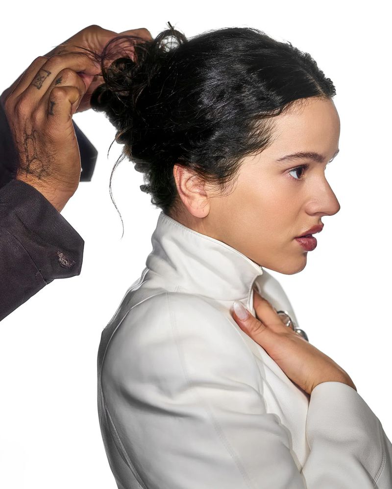 Profile view of a stylish woman having her dark hair styled. She wears a white jacket with a hand at her collar.