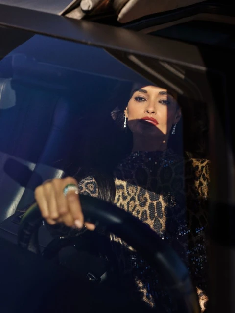 Elegant woman with red lipstick driving a car with a leopard print top. Car interior, posing, fashion portrait, diamond earrings, and ring.