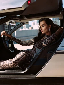 Model Gizele Oliveira wearing a leopard print jumpsuit seated inside a car with gullwing doors for Elle Slovenia.