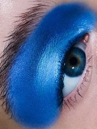 Close-up of a woman's eye with blue eyeshadow. The eye has a bright blue iris, dark lashes, and a bold, solid application of eyeshadow.